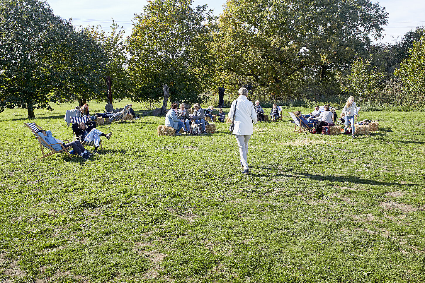 Personen sitzen auf Stühlen unk Bänken auf einer Wiese