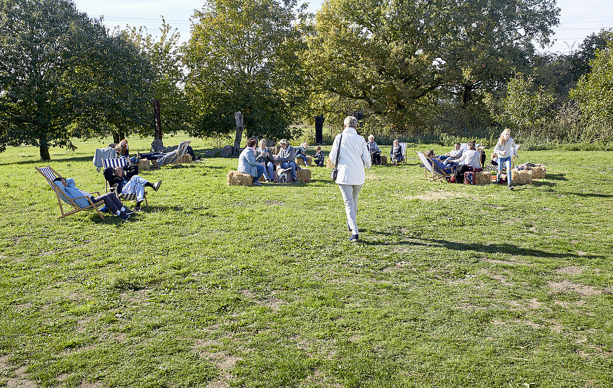 Personen sitzen auf Stühlen unk Bänken auf einer Wiese