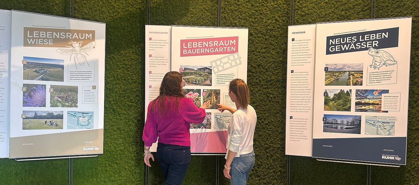 Zwei Personen schauen sich eine Thementafel zum Lebensraum Bauerngarten an