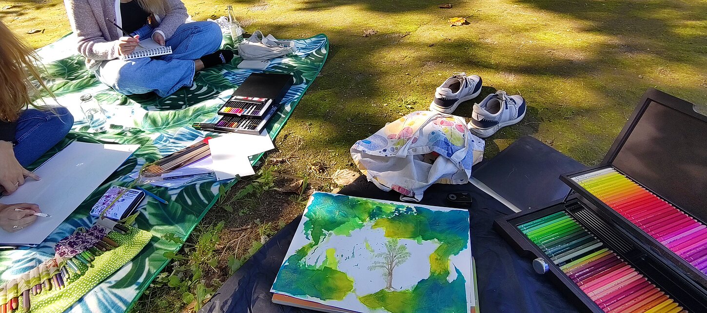 Es wird draußen auf einer Picknickdecke mit bunten Farben gemalt.
