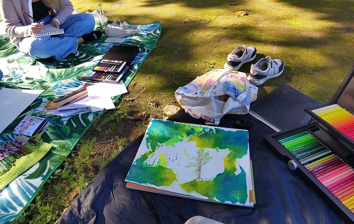 Es wird draußen auf einer Picknickdecke mit bunten Farben gemalt.