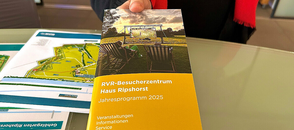 Ein Gast bekommt das Jahresprogramm 2025 vom Haus Ripshorst überreicht