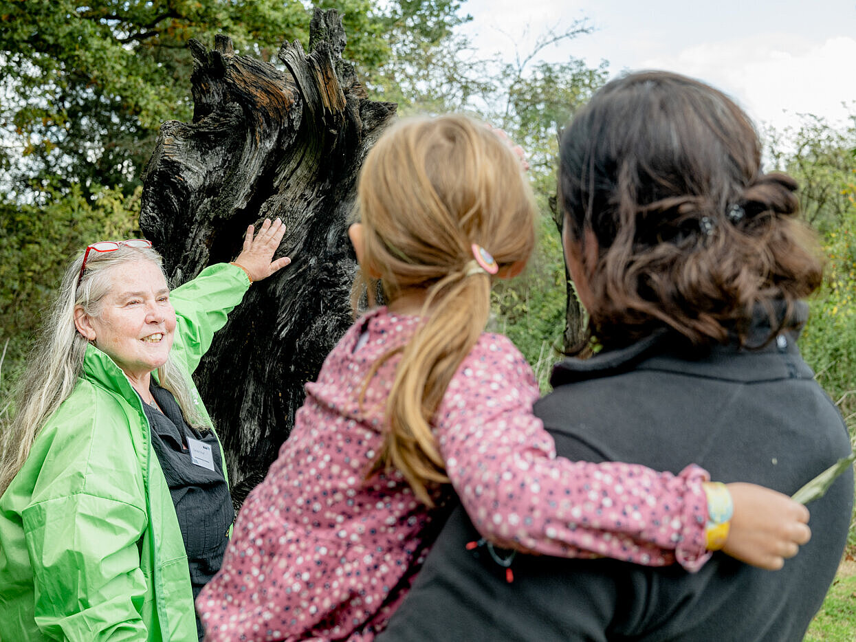 Eine Frau zeigt auf einen Baum. Zwei Personen schauen zu.