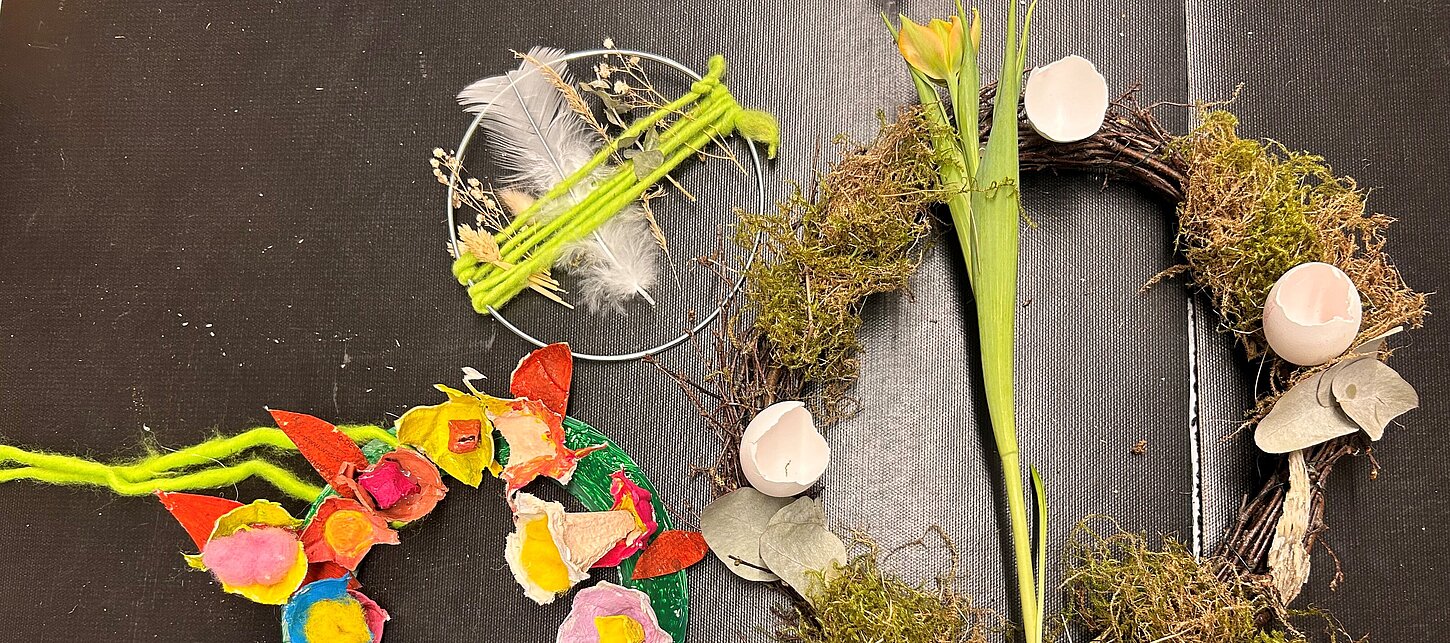 Drei fertige, bunte Osterkränze liegen auf dem Tisch.