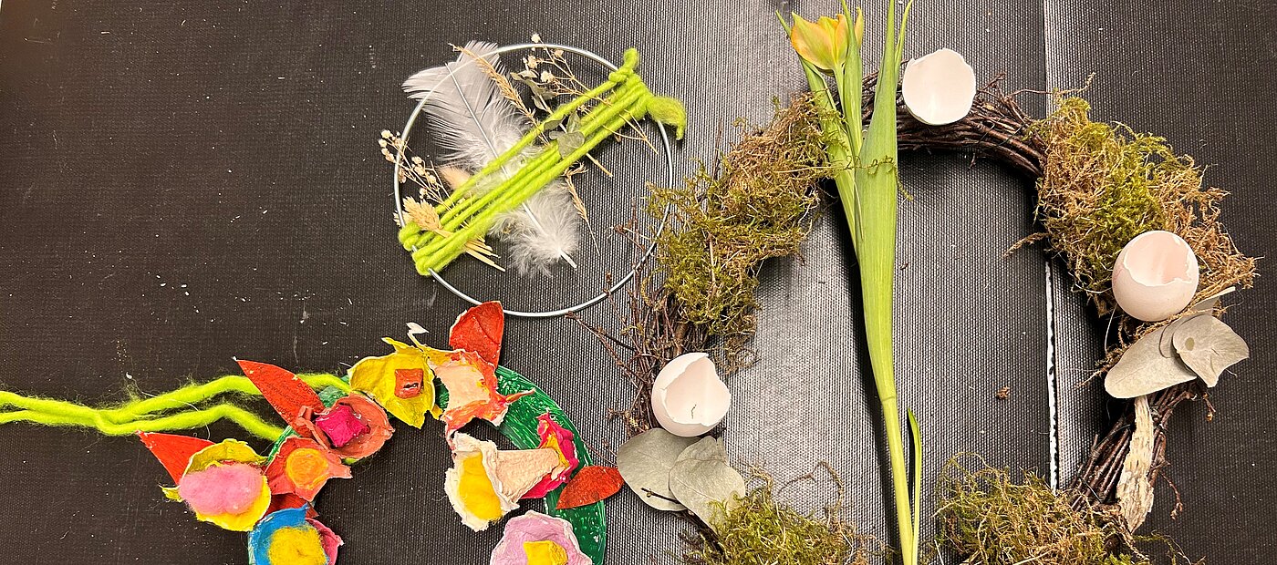 Drei fertige, bunte Osterkränze liegen auf dem Tisch.