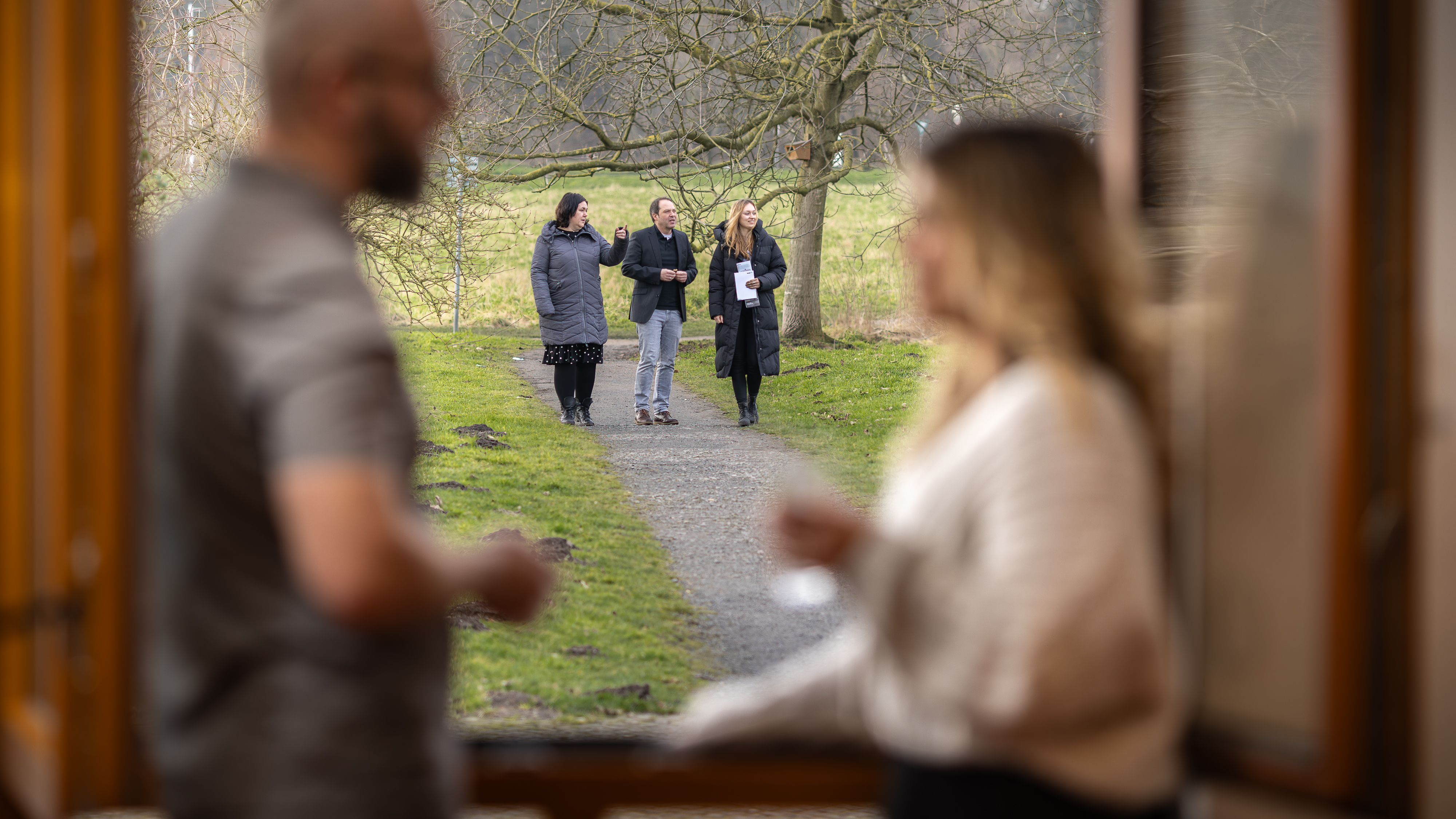Zwei Personen im Seminarraum unterhalten sich in der Pause. Im Hintergrund gehen 3 Personen spazieren