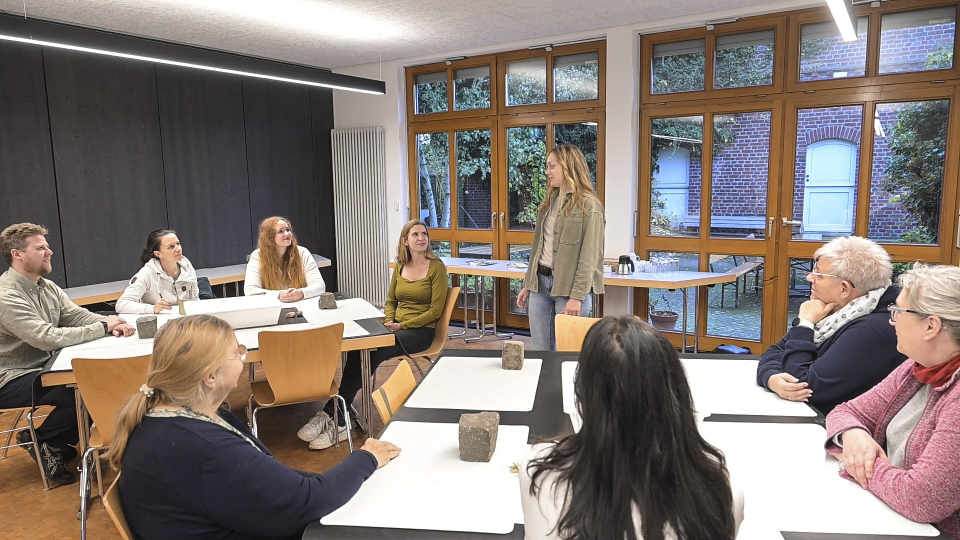 Kursleiterin erklärt in die Runde den Menschen die am Tisch sitzen etwas