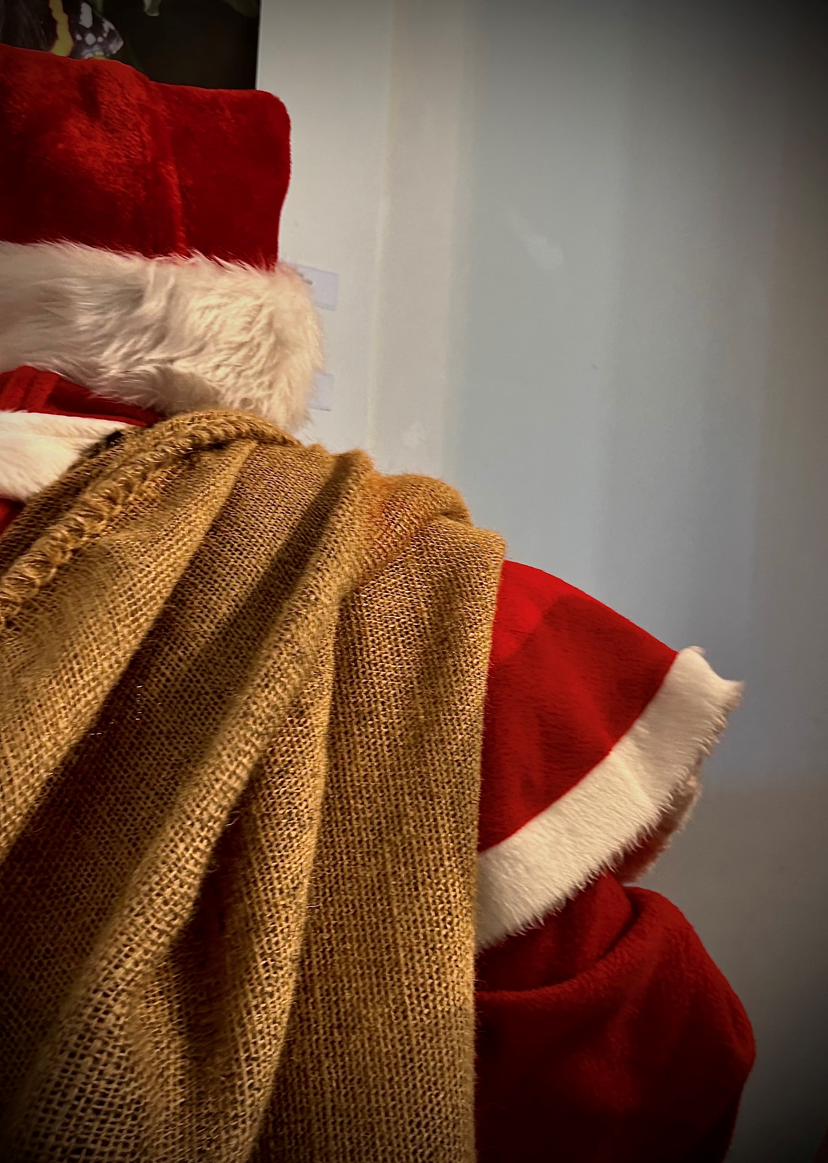 Ein Ausschnitt des Weihnachtsmanns von hinten. Man sieht seine rote Zipfelmütze, sein Geschenkesack hat er über den Rücken geworfen.